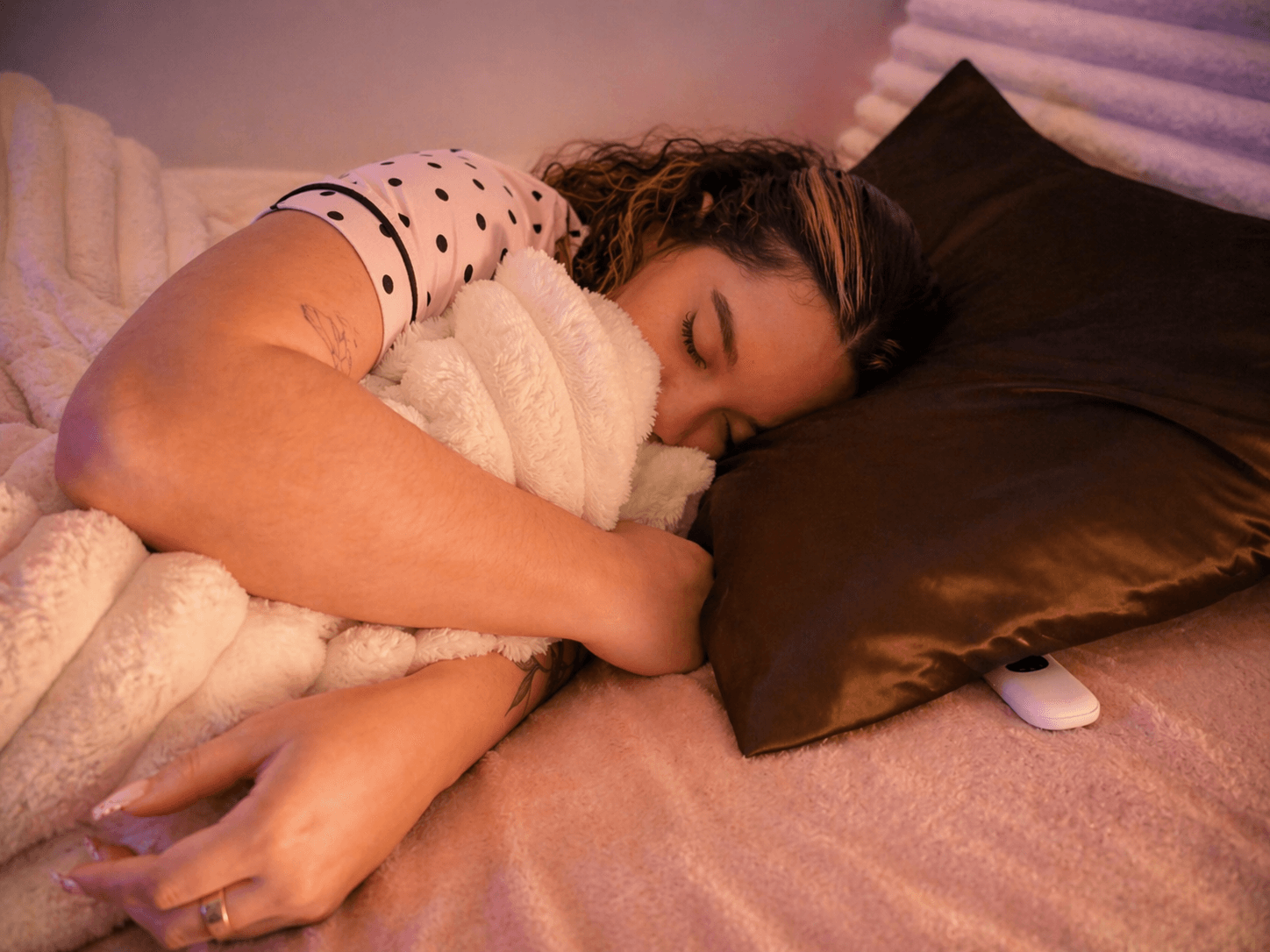A woman asleep on her side on a satin pillow, a white Lullabar at the pillow’s edge
