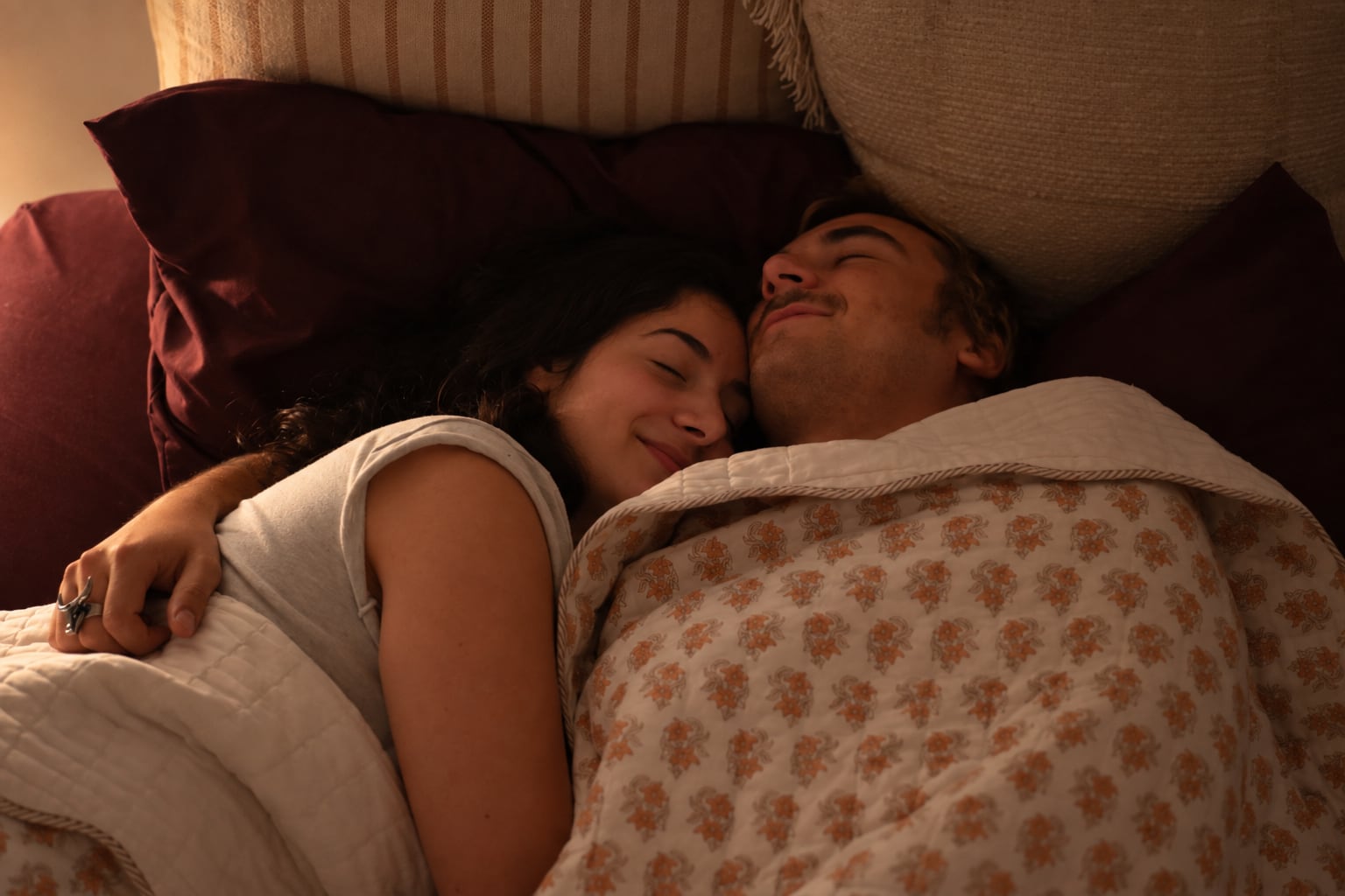 A couple asleep close together under a floral quilt.